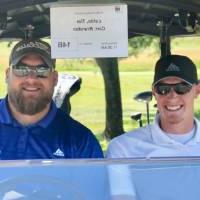 two alumni smile for picture in golf cart